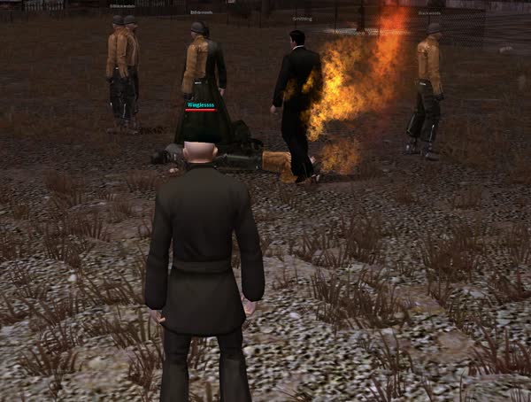 A gang member burns in a column of fire while an operative faces a group of thugs in an empty lot at dusk.